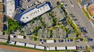 Aerial Exterior top down view, tops of buildings, trees places throughout the property, playground adjacent to leasing office.