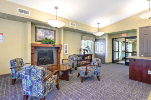Interior Community Dining hall, coffee table with four lounge chairs, fireplace bookcase right of fireplace, contemporary design, purple and tan patterned carpeting.