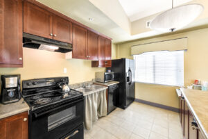 Interior community kitchen, black appliances, Dual stainless steel sink, brown cabinetry, laminate countertops.