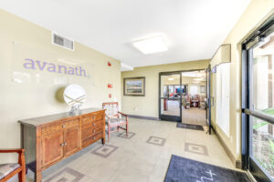 Interior Leasing Office lobby, Large Avanath signage above Large dresser, chairs, community dining hall to the right upon entering. Tile flooring.