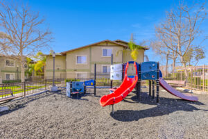 Exterior Playground, Soft Ground, Fenced in, Residential Buildings in the background, slides, benches, Street light inside playground area.